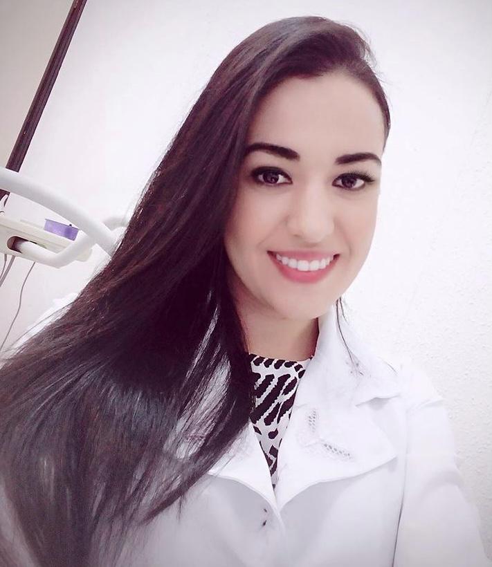 Dra. Raquel Mendes Barbosa, cirurgiã dentista, sorrindo de jaleco branco em consultório